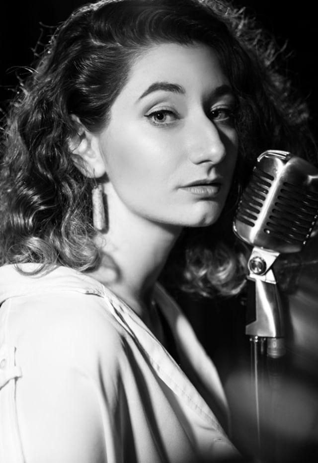 Yana Litinskaya beside a vintage microphone in a black and white portrait